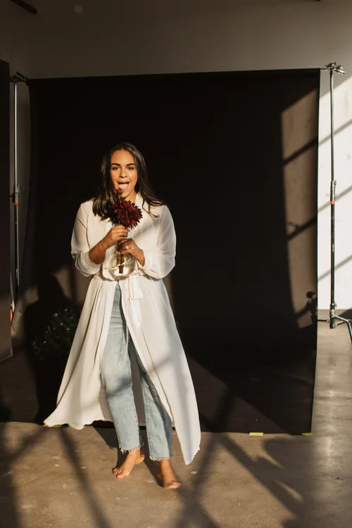 Woman in white cardigan holding red flowers against black backdrop