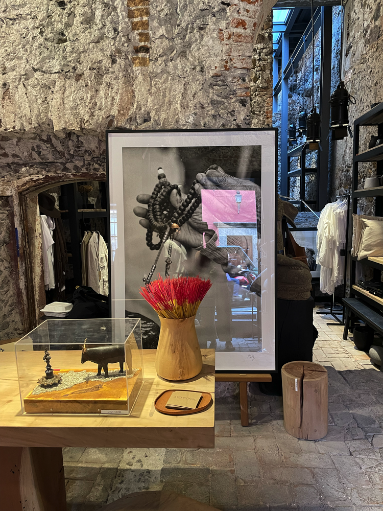 Boutique storefront displays artwork, wooden vase, and artisan crafts on rustic stone wall