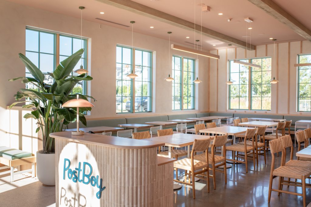 Modern restaurant interior with PostBoy branding, wooden chairs, large windows, pendant lighting