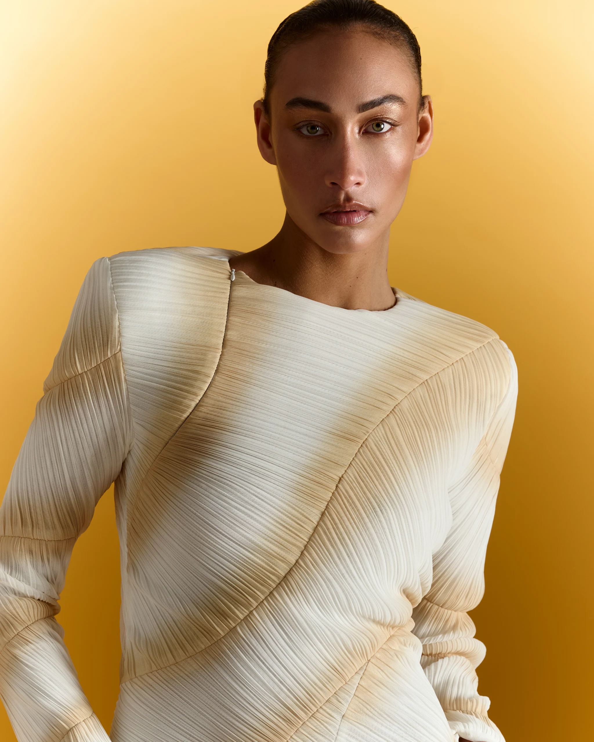 Portrait of woman wearing cream ribbed long-sleeve top against yellow background