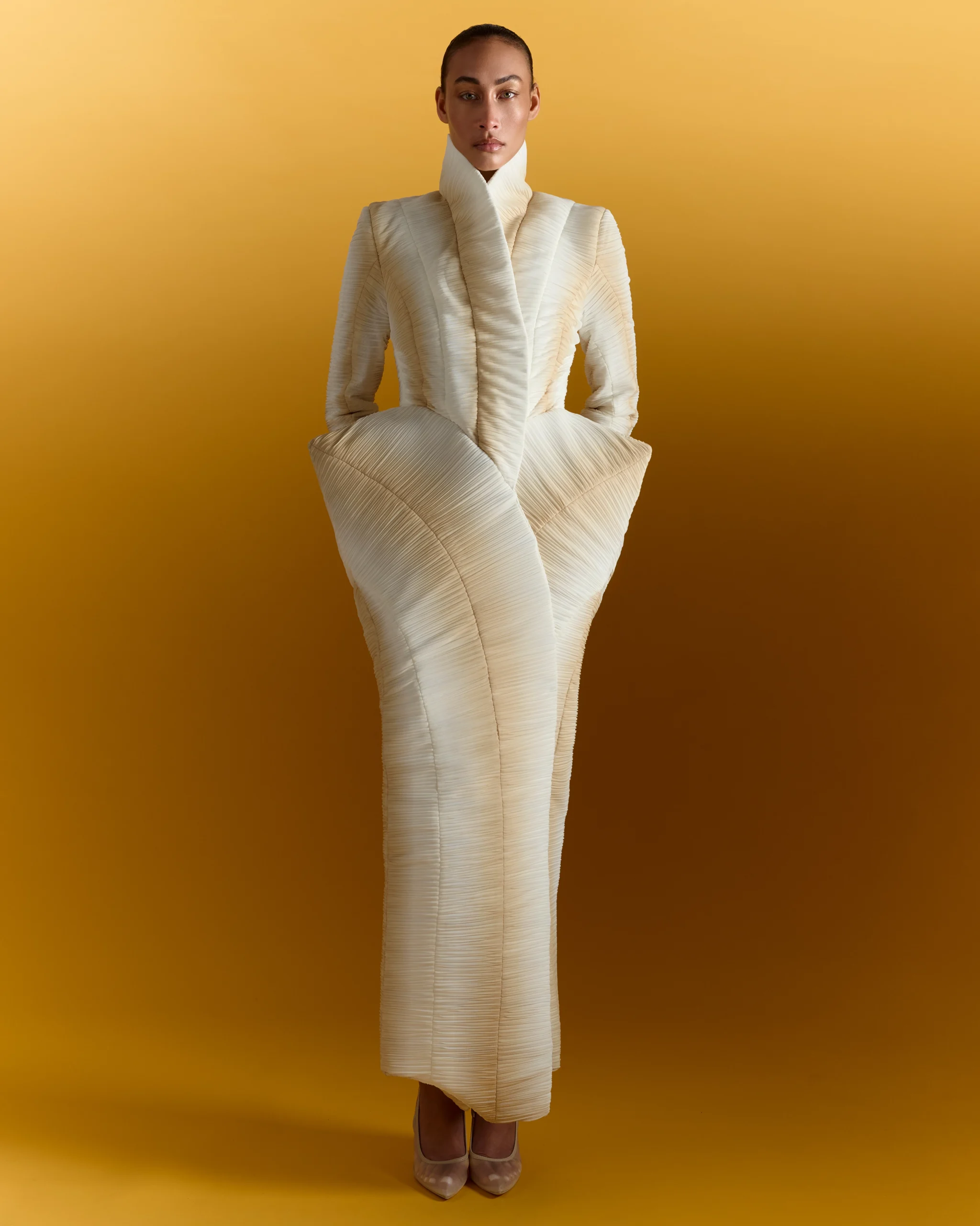 Woman wearing cream textured blazer and pleated skirt against yellow background