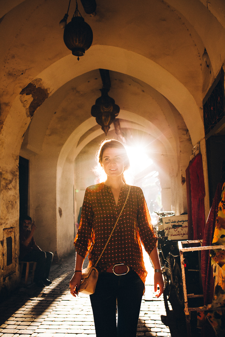Woman walking through sunlit arched alleyway with traditional architecture