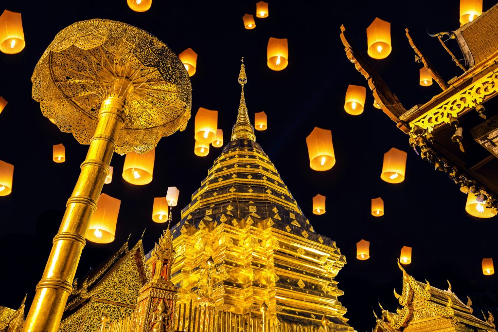Golden Buddhist temple at night with floating lanterns illuminating dark sky