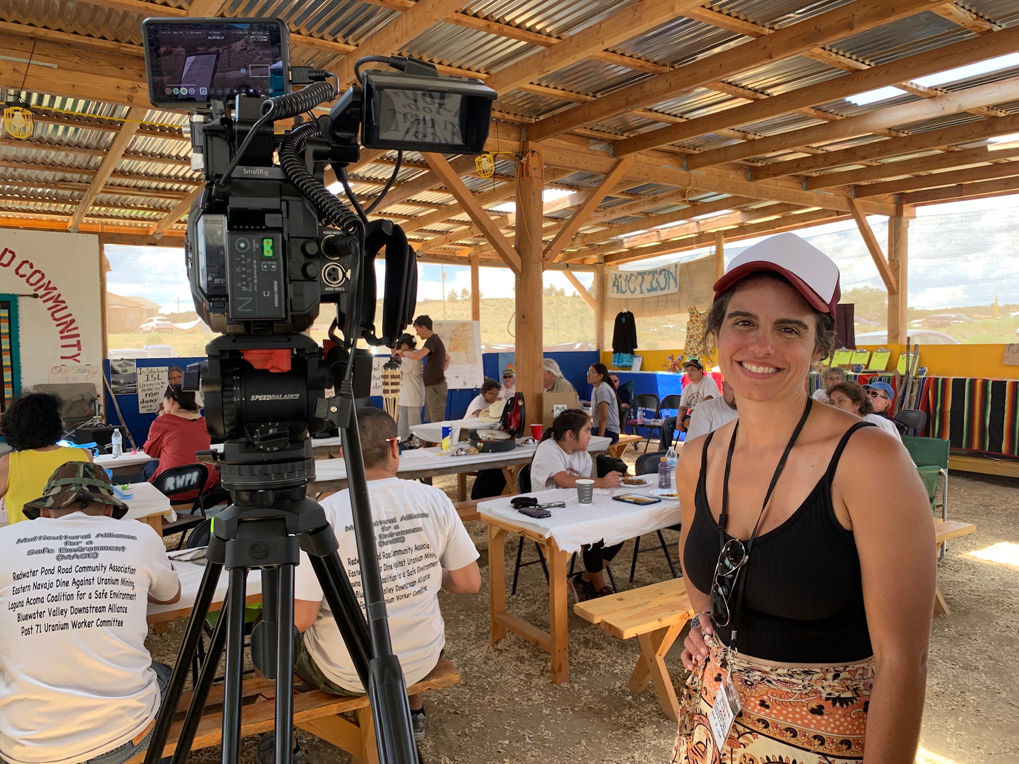 Image of a woman wearing a baseball cap, smiling next to a movie camera on set.