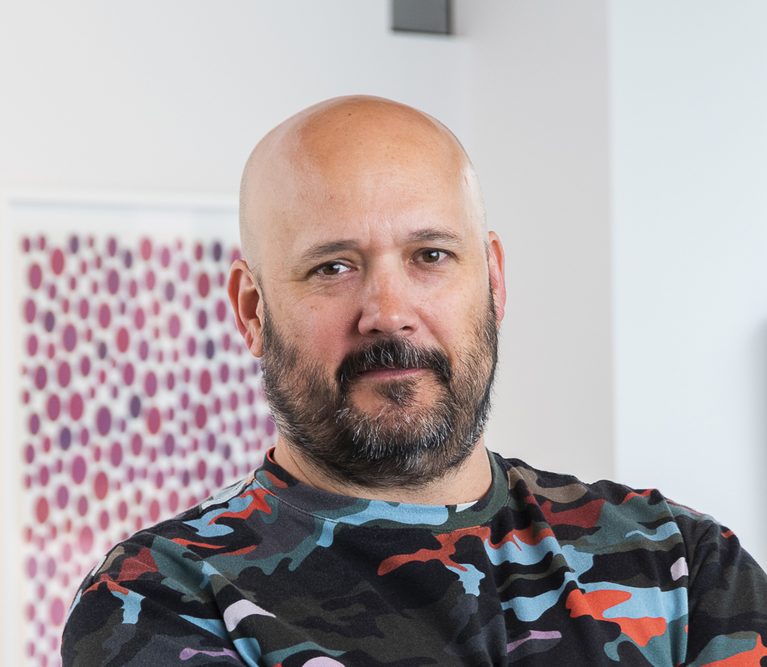headshot portrait of bald, bearded man wearing a brightly colored camo shirt